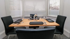 A corner dining area with a wooden table, black chairs, and a window with blinds. - Craven Suite (Scarborough)