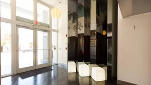 Un hall d’entrée moderne avec des portes en verre, un sol ciré et un espace détente avec des chaises blanches.