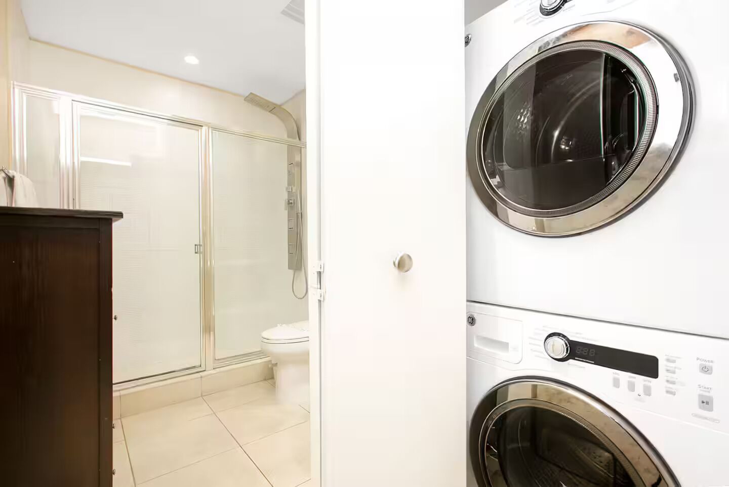 A bathroom with a glass shower enclosure, a toilet, and a stacked washer and dryer unit.