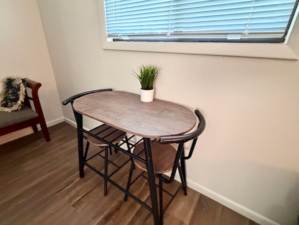 Une table à manger avec des chaises, une plante en pot et une fenêtre avec des stores.