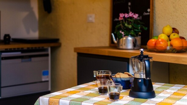 Eine Küchenzeile mit einer Kaffeemaschine, Tassen und einer Obstschale auf der Arbeitsplatte.