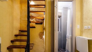 Eine Treppe mit Holzdielen und Metallgeländer, die zu einer Tür führt, durch deren Glasabtrennung eine Duschkabine zu sehen ist.