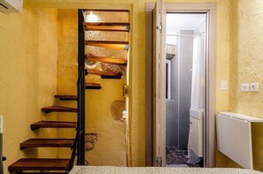 Eine Treppe mit Holzdielen und Metallgeländer, die zu einer Tür führt, durch deren Glasabtrennung eine Duschkabine zu sehen ist.