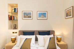 A neatly arranged hotel room with a bed, two bedside tables with lamps, a bookshelf, and two framed pictures on the wall. - San Trifone RiR Collection (Rome)