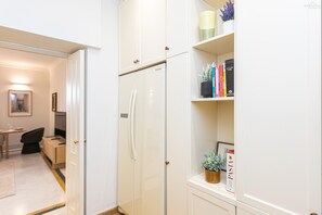 A compact kitchen with a white refrigerator, a small dining area with a table and chairs, and a bookshelf with books and decorative items. - San Trifone RiR Collection (Rome)