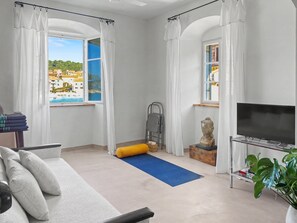 A living room with a sofa, a TV, a window with curtains, a blue mat, a statue, and a bookshelf. - Seafront — A Place Like No Other (Stari Grad)