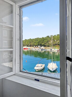 A window with a view of a marina, boats, and a forested hillside. - Seafront — A Place Like No Other (Stari Grad)