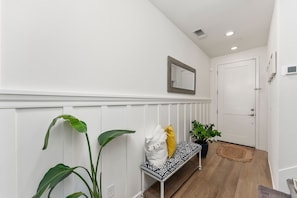 A hallway with a bench, a potted plant, a mirror, and a door. - Welcome  - Modern, North Sacramento Tropical Home (Sacramento)