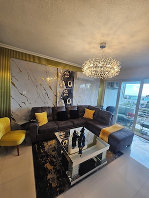 A modern living room with a sectional sofa, a glass coffee table, and a chandelier. - LUXURY 1 BEDROOM APT  NEW KINGSTON  WITH 24 HRS SECURITY, GYM AND ROOF TOP POOL (Kingston)