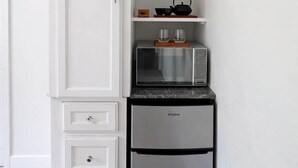 Een kleine keuken met een ingebouwde magnetron, broodrooster en koelkast, plus een klein plankje en een kastje.
