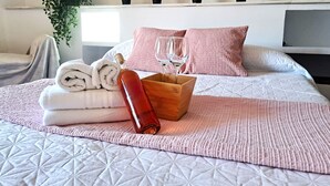 A neatly made bed with rolled towels, a bottle, and glasses on a pink bedspread.