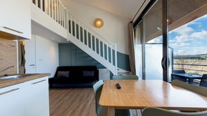A modern interior with a wooden dining table, a staircase, a black sofa, and a view through large windows. - Appart Hôtel les Lofts du Grand Lac (Langogne)