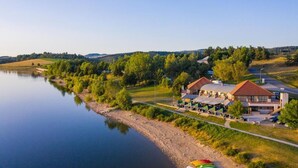 A lakeside hotel with a large building, a dock, and a boat. - Appart Hôtel les Lofts du Grand Lac (Langogne)