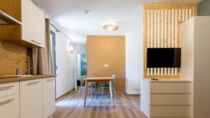 A compact kitchen with a dining area, wooden flooring, and a built-in TV. - Appart Hôtel les Lofts du Grand Lac (Langogne)