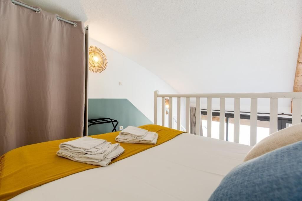 A bedroom with a bed, a yellow bedspread, white towels, a white railing, and a wall-mounted light fixture.