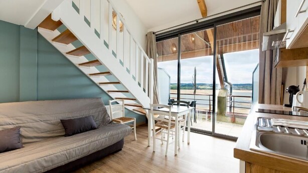 A modern interior with a staircase, a sofa, a dining area, and a view through a large window. - Appart Hôtel les Lofts du Grand Lac (Langogne)