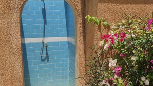 A blue-tiled shower enclosure with a hose, surrounded by a textured wall and flowering plants. - Superb villa with private pool & wooded garden 500m from the beach in Nianing  (Nianing)