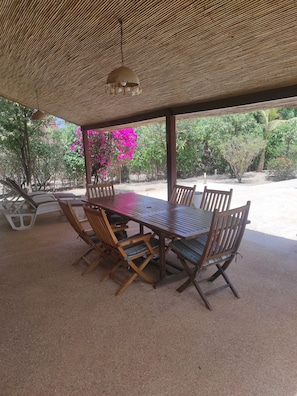 An outdoor covered dining area with a wooden table and chairs, surrounded by greenery and a clear view of the outdoors. - Superb villa with private pool & wooded garden 500m from the beach in Nianing  (Nianing)