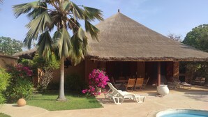 A thatched-roof building with a pool, lounge chairs, and a palm tree. - Superb villa with private pool & wooded garden 500m from the beach in Nianing  (Nianing)