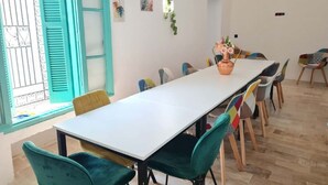 Uma sala de jantar com uma mesa comprida, cadeiras azul-turquesa e uma janela com persianas azuis.