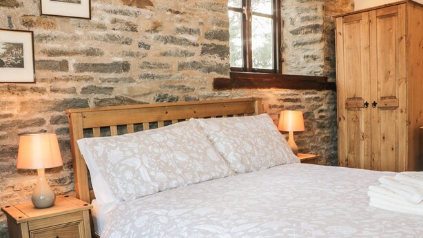 Ein Schlafzimmer mit Steinwand, hölzernem Bettgestell, floralem Bettzeug, zwei Nachttischlampen, einem Nachttisch aus Holz und einem Holzschrank.
