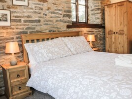 A bedroom with a stone wall, wooden bed frame, floral bedding, two bedside lamps, a wooden nightstand, and a wooden wardrobe.