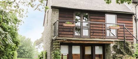 A two-story building with a balcony, a gravel driveway, and greenery around.