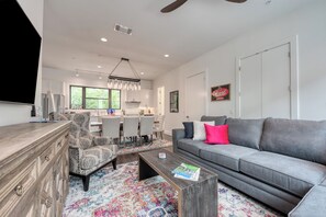 A modern living room with a grey sofa, patterned armchair, coffee table, and a dining area with a chandelier.