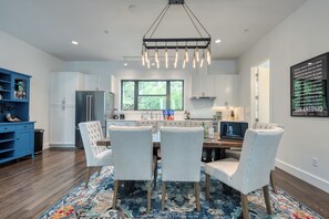 A modern kitchen with white cabinets, a dining area with four chairs, a large window, and a hanging light fixture.