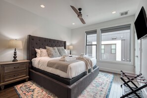 A bedroom with a large bed, a ceiling fan, a TV, and a window.