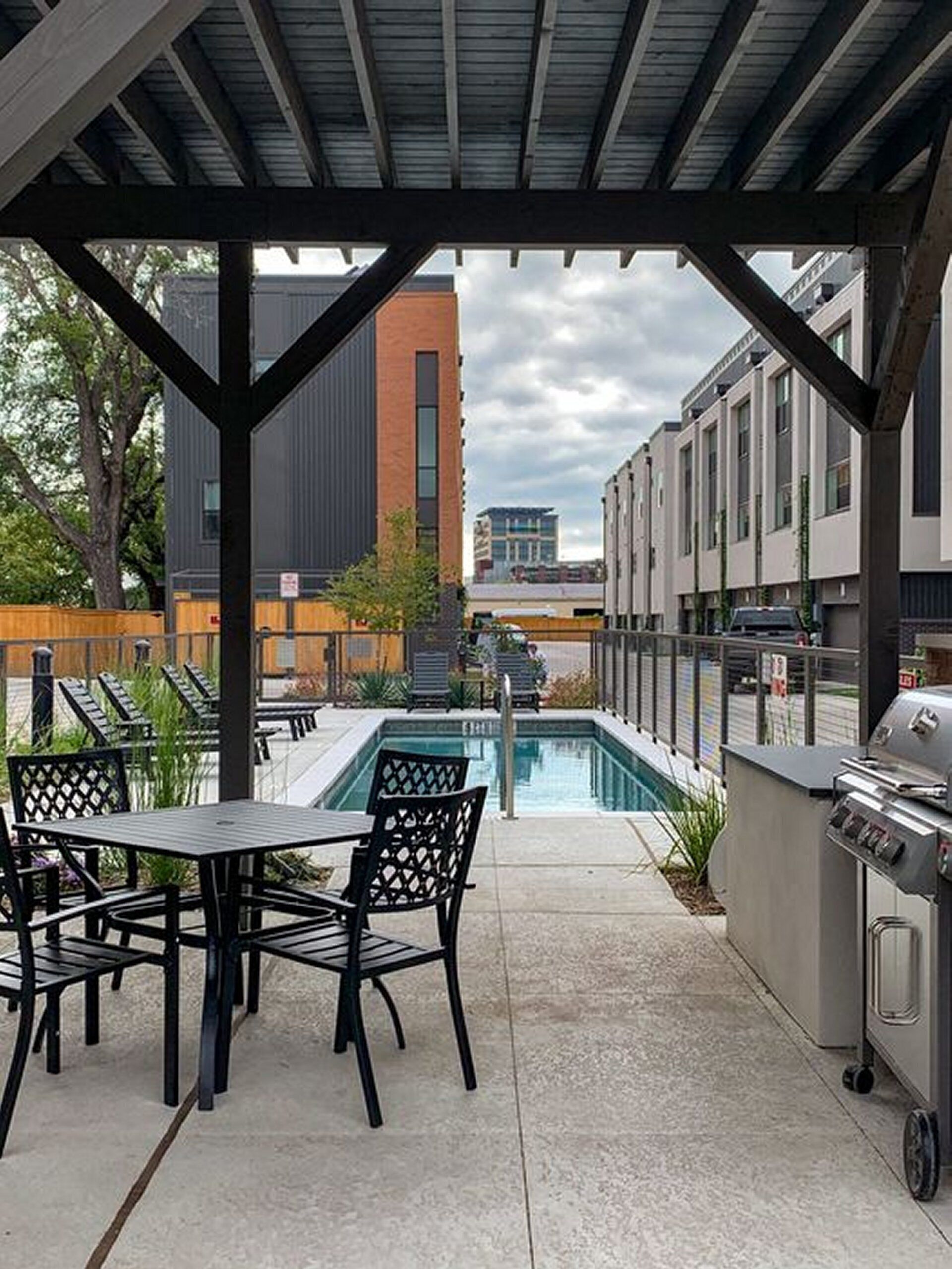 An outdoor patio with a pool, a grill, and a view of buildings in the background.