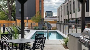 Une terrasse extérieure avec une piscine, un barbecue et une vue sur les bâtiments en arrière-plan.