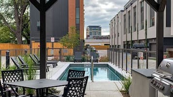 An outdoor patio with a pool, a grill, and a view of buildings in the background.