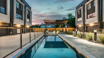 A modern pool area with a pergola, two-story buildings, and a clear sky.