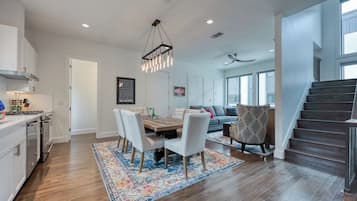 A modern kitchen with a dining area, a staircase, and a living room with a sofa and patterned armchair.