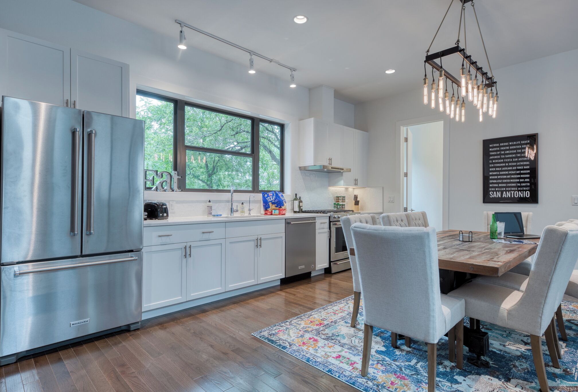 A modern kitchen with stainless steel appliances, a large window, and a dining area with a wooden table and chairs.