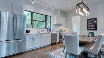 A modern kitchen with stainless steel appliances, a large window, and a dining area with a wooden table and chairs.