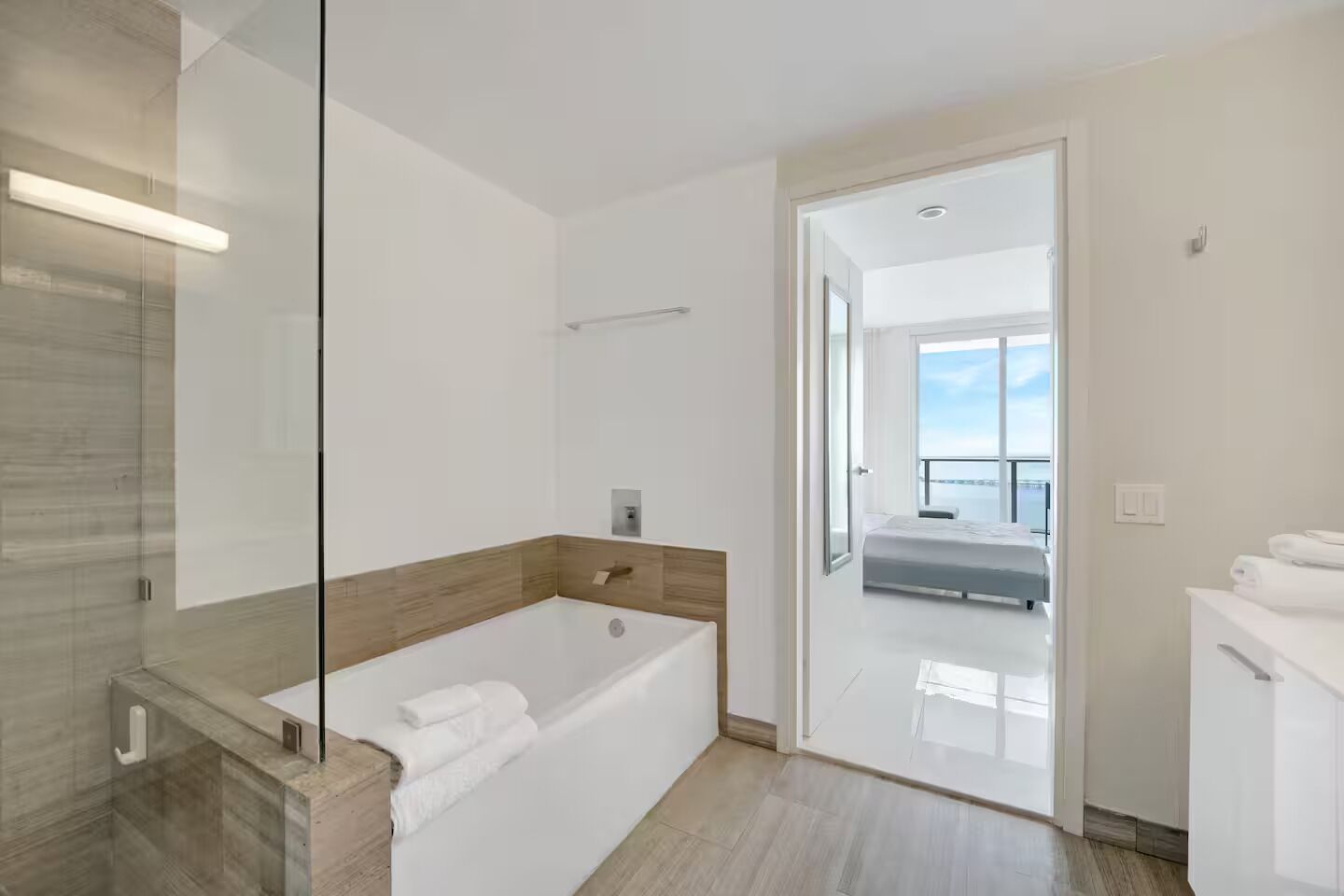 A modern bathroom with a large bathtub, a glass shower enclosure, and a view of a balcony.