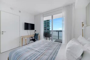 Ein modernes Hotelzimmer mit einem Bett, einem Schreibtisch mit Stuhl, einem an der Wand montierten Fernseher und einem Balkon mit Blick auf die Stadt.