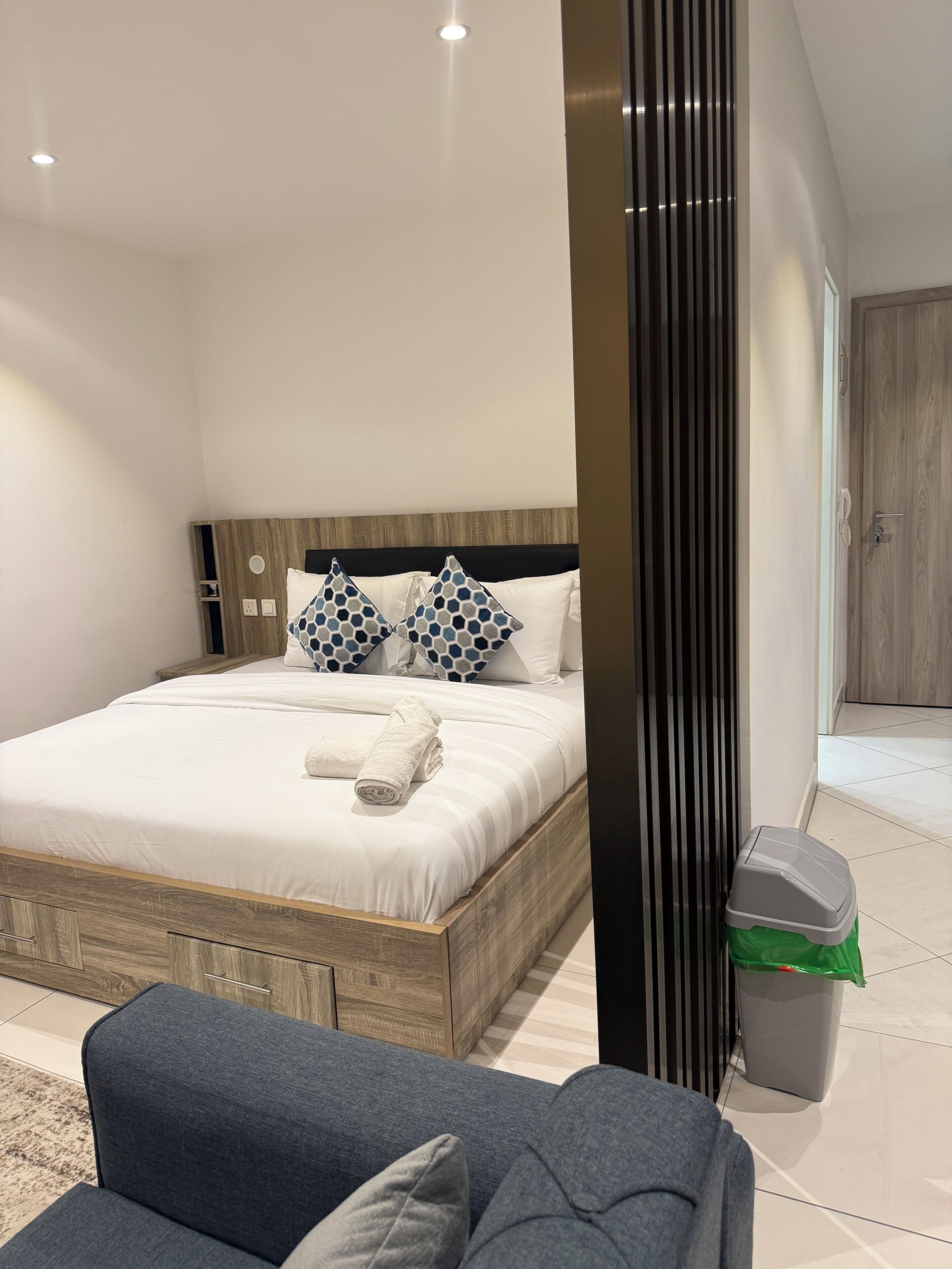 Ein modernes Schlafzimmer mit einem hölzernen Bettgestell, einem grauen Sofa und einem Mülleimer.