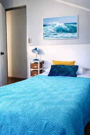 A bedroom with a bed, a nightstand, a lamp, a wall-mounted picture, and a door.