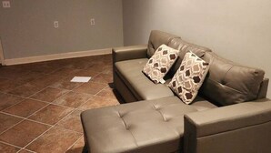 Ein Wohnzimmer mit Sofa, Hocker, Fliesenboden und einer Decke mit Einbauleuchten.