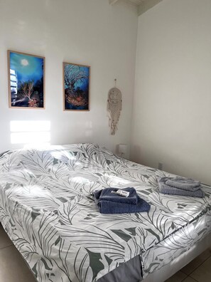 Ein Bett mit Bettdecke mit Blattmuster, zwei gerahmte Bilder an der Wand und ein Traumfänger.