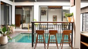 A pool area with wooden chairs, a railing, and potted plants. - Cozzy Villa Devine (Canggu)
