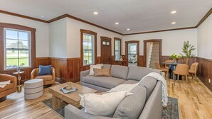 A spacious living room with a large gray sectional sofa, a wooden coffee table, and a dining area with a small table and chairs.