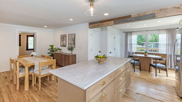 A modern kitchen with wooden flooring, a marble island, and a dining area with wooden furniture.