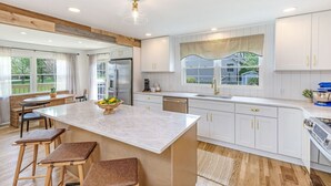 A kitchen with a large island, white cabinetry, and a view of the outdoors.