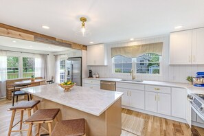 A kitchen with a large island, white cabinetry, and a view of the outdoors.