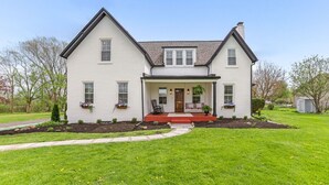 A two-story house with a front porch, a small garden, and a pathway leading to the entrance.