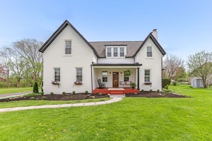 A two-story house with a front porch, a small garden, and a pathway leading to the entrance.